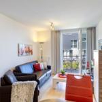 Wohnzimmer mit Sofa, Tisch und Balkonansicht. Rote Stühle und Wandbild.
