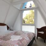 Schlafzimmer mit Dachschrägen, Bett, Stuhl und Fenster mit Blick auf Bäume.