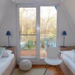 Zwei Betten mit Streifenkissen, weiße Stuhle und blau leuchtende Lampen vor großem Fenster mit Blick auf Wald.