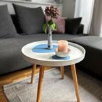 Runder Tisch mit Blumenvase und Kerze vor grauem Sofa