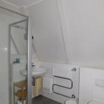 Badezimmer mit Dusche, Waschbecken und Toilette. Dachschrägen und Handtuchhalter sichtbar.
