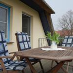 Terrasse mit Holztisch, drei Stühlen und Blumen im Vase.