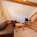 Wohnbereich mit braunem Sofa, Holztisch und Holztreppe