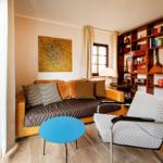 Wohnzimmer mit Sofa, Sessel, Tisch und Bücherregal. Fenster mit Vorhängen.