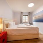 Schlafzimmer mit Bett, Nachttisch und Wandbild. Fenster mit Vorhängen.