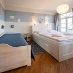 Zimmer mit zwei Betten, Holzboden und Fenster mit Vorhängen.