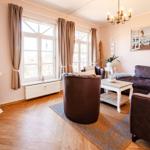 Wohnzimmer mit Sofa, Sessel, TV und Fenstern mit Vorhängen.
