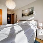 Schlafzimmer mit Doppelbett, Nachttisch und Wandbild. Deckenleuchte und Holztür sichtbar.