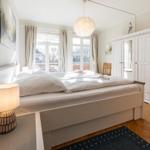 Schlafzimmer mit Doppelbett, Kleiderschrank und Fenster zum Balkon.