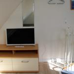 TV auf Holzregal, Spiegel an der Wand, weißer Kleiderständer und Bild