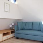 Ein blaues Sofa steht neben einem Holzschrank mit Schubladen und einer Lampe.