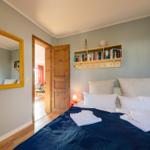 Schlafzimmer mit Bett, Spiegel und Bücherregal. Tür führt in angrenzenden Raum.