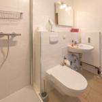 Badezimmer mit Dusche, Waschbecken und Toilette. Holztür und weiße Fliesen.
