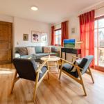 Wohnzimmer mit Sofa, zwei Stühlen und TV. Holzboden und große Fenster.