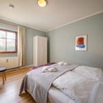 Schlafzimmer mit Bett, Kleiderschrank und Fenster mit Vorhängen.