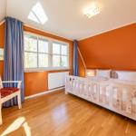 Schlafzimmer mit Holzbett, Fenster, Vorhängen und Holzboden.