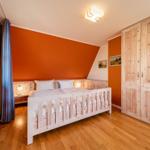 Schlafzimmer mit Holzbett, Kleiderschrank und Fenster. Wände orange, Holzboden.