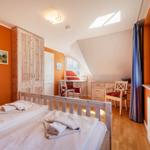 Schlafzimmer mit Doppelbett, Schreibtisch und Fenster. Holzmöbel und orange Wandfarbe.