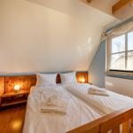 Schlafzimmer mit Doppelbett, Holzmöbel und Fenster. Decke geneigt, Licht durch Fenster.
