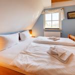 Zimmer mit Doppelbett, Fenster und Holzmöbel.