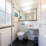 Badezimmer mit Toilette, Waschbecken und Dusche. Fenster mit getöntem Glas.