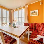 Esszimmer mit Holztisch, Sitzbank und Fenstern. Wandfarbe orange.