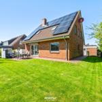 Ein Haus mit Solarpanelen auf dem Dach und einem großen Garten mit Terrasse.