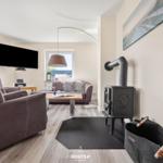 Wohnzimmer mit Sitzgelegenheiten, Kaminofen und Fernseher an der Wand.