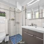 Badezimmer mit Dusche, Waschbecken und Toilette. Fliesen und Spiegel sind sichtbar.