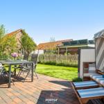 Terrasse mit Tisch, Stühlen und Strandkorb. Grünfläche und Häuser im Hintergrund.