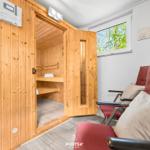 Sauna mit Holzverkleidung und Sitzbänken. Rote Sessel und Fenster mit Blick auf Bäume.