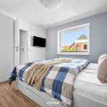 Schlafzimmer mit Bett, Kleiderschrank und Fenster zum Hausblick.