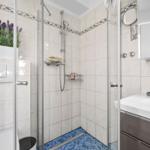 Dusche mit Glaswand, blauem Mosaikboden und weißen Fliesen.