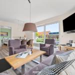 Wohnzimmer mit Sofa, Sesseln und TV. Durchgang in Schlafzimmer. Blick auf Garten.