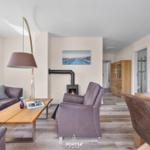 Wohnzimmer mit Sofa, Sessel, Kamin und Essbereich. Holzfußboden und Wandbilder.