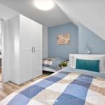 Schlafzimmer mit Dachschrägen, weißer Kommode und Bett mit blau-beigem Quilt.