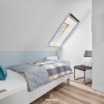 Schlafzimmer mit Dachfenster, Bett, Stuhl und Spiegel an der Wand.
