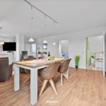 Wohn- und Essbereich mit Holzboden, Esstisch und Sofa. Im Hintergrund ist ein Schlafzimmer sichtbar.