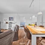 Essbereich mit Holztisch und Stühlen. Im Hintergrund Wohnbereich mit Kamin und Schlafzimmer.