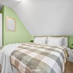 Schlafzimmer mit Bett, Kleiderschrank und Nachttisch. Wandfarbe grün, Holzboden.