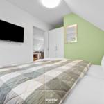 Schlafzimmer mit Bett, Fernseher und grünem Wandabschnitt