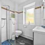 Badezimmer mit Dusche, Toilette und Waschbecken. Fenster mit getöntem Glas.