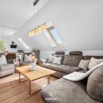 Wohnbereich mit Sofa, Sessel und Holztisch unter Dachschrägen mit Dachfenstern.