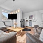 Wohnzimmer mit Sofa, Sessel, Holztisch und Fernseher an der Wand.