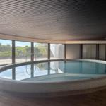 Runder Innenpool mit Glaswänden und Holzdecke. Außenbereich sichtbar.