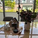 Esstisch mit Blumenvase, Gewürzdosen und Servierplatte vor großem Fenster