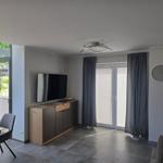 Wohnzimmer mit TV, Schrank, Fenstern und Vorhängen.
