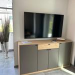 Flachbildfernseher über einem Schrank mit Holzoberfläche und grauen Türen.