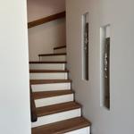 Treppe mit Holzstufen und weißen Wänden. An der Wand hängen zwei dekorative Elemente.