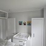 Schlafzimmer mit Wickelkommode, Kleiderschrank und Wandbildern von Tieren.